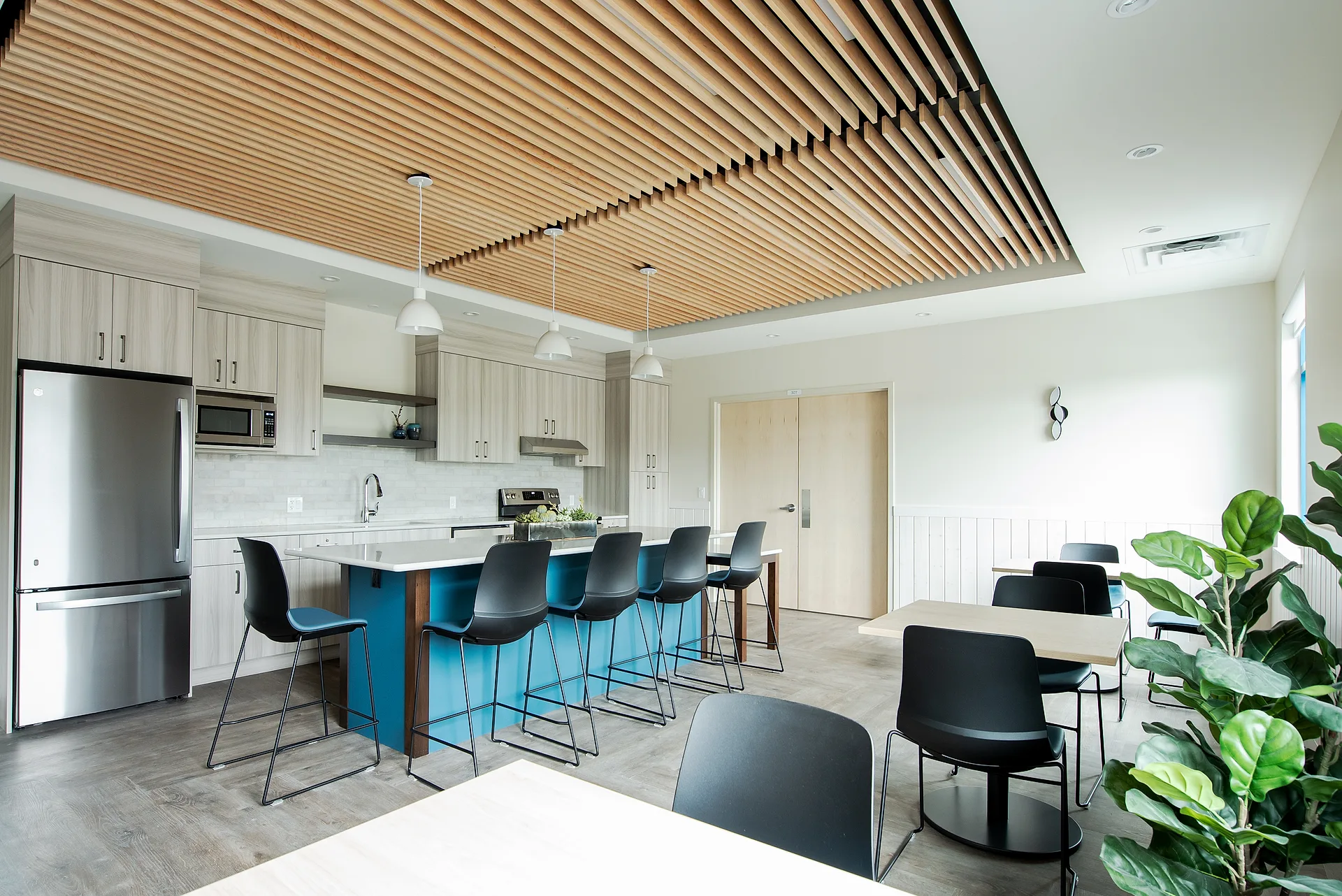 NONA Child Development Centre common kitchen with a slatted timber ceiling, island seating, and flexible dining tables